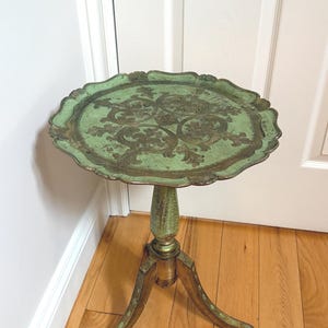 Peut inclure: Une table ronde sur pied avec un plateau à bord festonné présentant une finition vert clair vieillie et des motifs de volutes dorés. La colonne centrale et les trois pieds incurvés sont peints dans un style vert et doré assorti.
