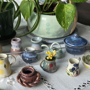 May include: A collection of miniature ceramic vessels including pitchers, vases, and bowls with various patterns like lemons and berries, arranged with a clear plastic ruler showing measurements in centimetres, ranging from 1 to 30 centimetres in length.