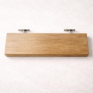 Puede incluir: Una estanter&iacute;a rectangular de madera con un acabado de vetas naturales. La estanter&iacute;a est&aacute; soportada por dos soportes met&aacute;licos. La estanter&iacute;a mide aproximadamente 61 cm de largo y 15 cm de ancho.