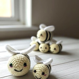 May include: Handmade crochet bees in various sizes. The bees are yellow with black stripes and white wings. Each bee has a smiling face with rosy cheeks. The bees are arranged on a light-colored wooden surface.
