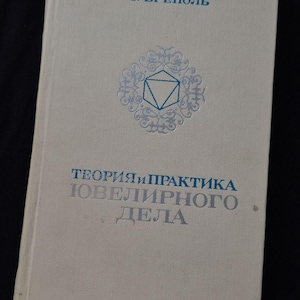 May include: A white hardcover book titled "Э. БРЕПОЛЬ" and "ТЕОРИЯ И ПРАКТИКА ЮВЕЛИРНОГО ДЕЛА" in blue text. The cover features a central blue geometric icon of a icosahedron surrounded by an intricate, circular, filigree-style pattern.