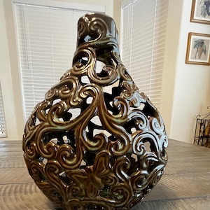 May include: A decorative brown ceramic vase with an openwork design featuring swirling patterns and butterfly accents. The vase has a glossy finish and a bulbous shape, suitable for home decor.