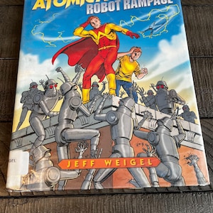 May include: A hardcover book titled "Atomic Ace and the Robot Rampage" with a colorful illustration. The cover features a superhero in a red and yellow suit, battling robots. The author's name, Jeff Weigel, is also visible.