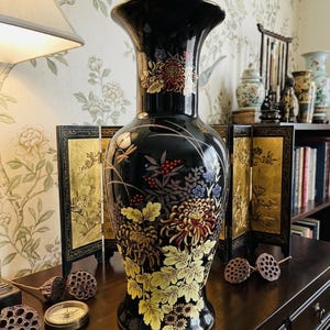 May include: A tall, black ceramic vase featuring a flared rim and a tapered neck. The body is decorated with detailed, multi-colored floral patterns, including yellow, red, and blue chrysanthemums, green leaves, and small red berries.