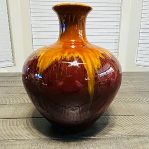 May include: A ceramic vase with a bulbous body and a narrow neck, featuring a glossy finish with a deep burgundy base color that transitions into a vibrant yellow drip pattern extending from the rim down toward the center of the vessel.