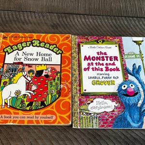 May include: Two vintage children's books. The first, "Eager Reader: A New Home for Snow Ball," features a king and horse illustration. The second, "The Monster at the End of This Book," stars Grover from Sesame Street. Both books are on a wooden surface.