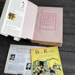 May include: An open vintage book with a pink interior and a pink "EX LIBRIS" stamp. A Reader's Digest magazine cover with the title "Dear Reader" and an illustration of a cafe is visible.