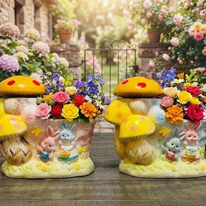 May include: Two ceramic planters shaped like mushrooms with yellow caps and red spots. The base features embossed figures of two rabbits and a butterfly. Each planter is filled with a colorful arrangement of artificial roses and small flowers.