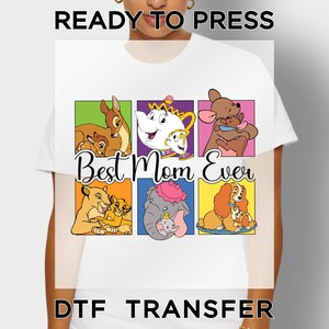 May include: White t-shirt with a colorful graphic featuring cartoon characters and the text "Best Mom Ever." The design includes images of Bambi, Mrs. Potts, Roo, Simba, Dumbo, and Lady. The words "READY TO PRESS" and "DTF TRANSFER" are also visible.
