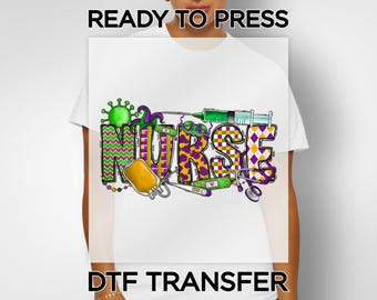 May include: White t-shirt with a colorful "NURSE" graphic. The design incorporates medical elements like a syringe, stethoscope, and IV bag, along with the text "READY TO PRESS" and "DTF TRANSFER". The letters are in various patterns and colors.