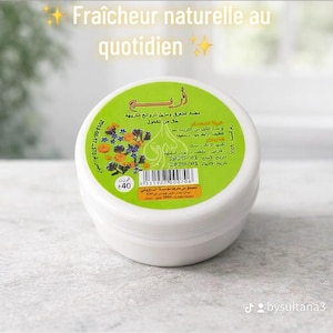 Peut inclure: Un contenant rond blanc de déodorant solide avec du texte en français et en arabe. L'étiquette indique "100% naturel" et "sans alcool". Le produit est étiqueté "Nouveauté!" et pèse 40 grammes.