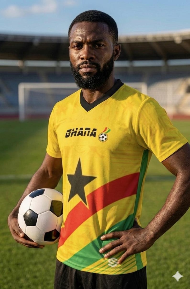 Pu&ograve; includere: Una maglia da calcio gialla con la scritta "GHANA" e una grafica di pallone da calcio. La maglia presenta una stella nera e strisce rosse, gialle e verdi. Un pallone da calcio &egrave; tenuto davanti alla maglia.