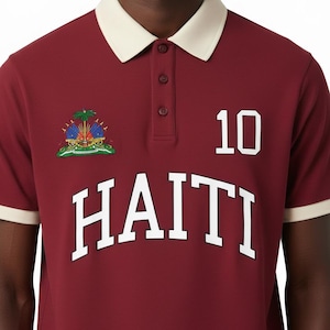 May include: Maroon polo shirt with a cream-colored collar and cuffs. Features the word "HAITI" in large white letters, the number "10", and a colorful emblem. A classic, sporty design.