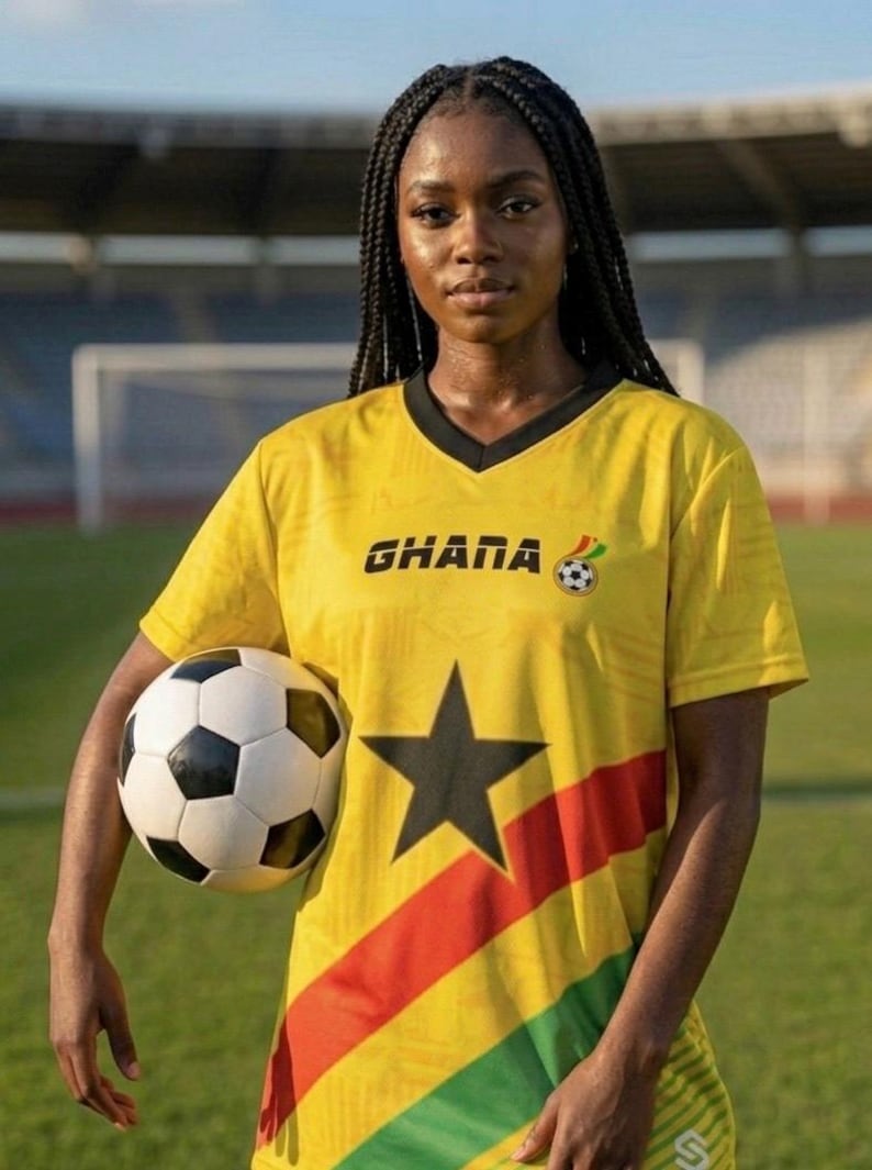 Pu&ograve; includere: Una maglia da calcio gialla con la scritta "GHANA" e una grafica di pallone da calcio. La maglia presenta una stella nera e strisce rosse, gialle e verdi. Un pallone da calcio &egrave; tenuto davanti alla maglia.
