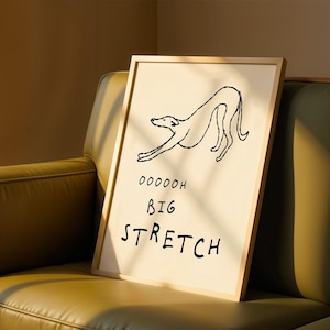 A framed poster with a simple drawing of a dog and the text "OODDOH BIG STRETCH" is displayed on a brown leather couch.