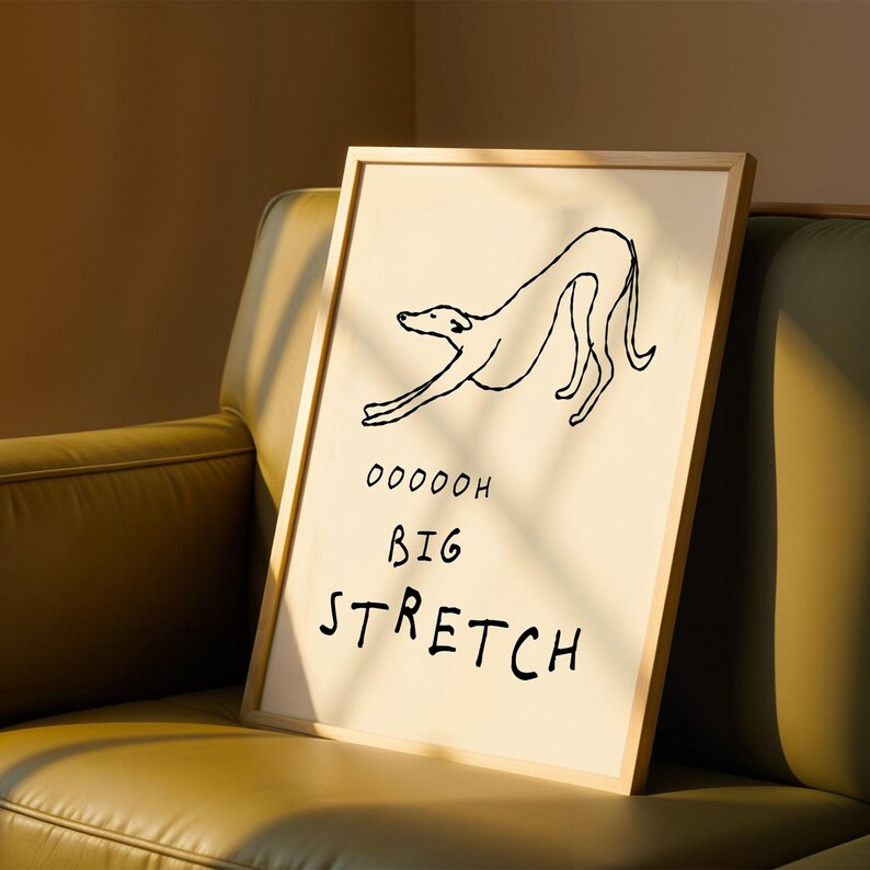 A framed poster with a simple drawing of a dog and the text "OODDOH BIG STRETCH" is displayed on a brown leather couch.