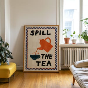 Puede incluir: Un cuadro rectangular enmarcado con fondo blanco y un borde a cuadros azules y naranjas. En el centro, una tetera naranja vierte líquido en una taza azul oscuro, con el texto negro "SPILL THE TEA" impreso alrededor de la ilustración.