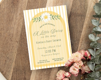Può includere: Invito per un baby shower a tema margherita. L'invito presenta strisce gialle e bianche, un'illustrazione di margherita e il testo "A Little Daisy on the way". L'invito è su una superficie di legno con fiori.