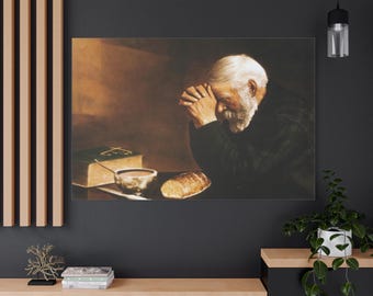 Puede incluir: Impresión en lienzo que representa a un anciano con barba y pelo blancos, con las manos juntas en oración. Un libro, un cuenco y pan están sobre la mesa. La obra de arte tiene una paleta de colores cálidos, sepia, que evoca reverencia y contemplación.