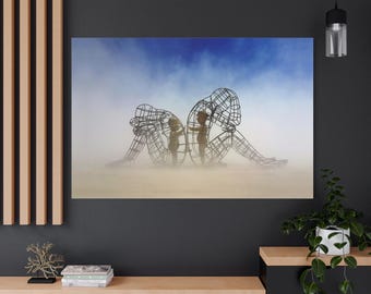 Puede incluir: Impresión en lienzo que presenta una escultura de alambre de dos figuras abrazándose, con dos figuras más pequeñas en el interior. El fondo tiene un cielo azul y un paisaje brumoso y arenoso. La obra evoca temas de conexión y apoyo.