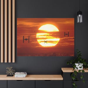 May include: A canvas print depicting a sunset scene with a large, bright yellow sun and orange clouds. Silhouetted TIE fighters are visible, with a few small ships in the sky. The artwork evokes a sense of adventure and space.