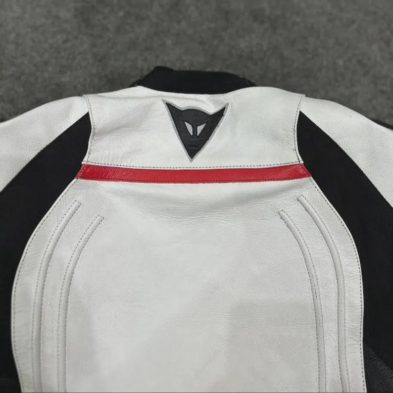 Puede incluir: Chaqueta de moto de cuero blanco y negro con una franja roja en la espalda. La chaqueta presenta un cuello negro y un logotipo en la parte superior de la espalda. Las costuras son visibles y la chaqueta parece estar hecha de cuero de alta calidad.