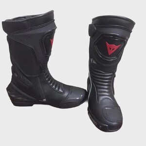 May include: Pair of black motorcycle boots with red accents. The boots have a tall design, a zipper closure, and a reinforced toe. The boots feature a red logo on the side and are designed for protection and performance.