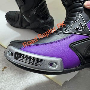 Może przedstawiać: Czarne i fioletowe buty motocyklowe ze srebrnym ochraniaczem palc&oacute;w. Buty mają markę "DAINESE". Zaprojektowane do jazdy na motocyklu, zapewniają ochronę i styl.