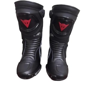 May include: Pair of black motorcycle boots with a red logo on the shin. The boots have a sleek design with reinforced areas and a ridged lower section. The boots are designed for protection and performance.