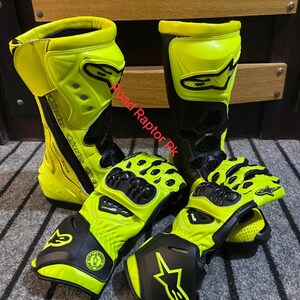 May include: A pair of neon yellow and black motorcycle boots and gloves. The boots are tall, with a prominent yellow shin guard and black accents. The gloves have a similar design, with black knuckle protection and yellow detailing. The text "Road Raptor PK" is visible.