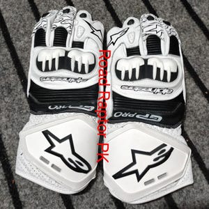 Könnte beinhalten: Paar weiße und schwarze Motorradhandschuhe mit dem Text "Road Raptor PK". Die Handschuhe haben ein Sternlogo und den Markennamen "Alpinestars". Die Handschuhe haben Schutzfunktionen an Knöcheln und Handgelenk.