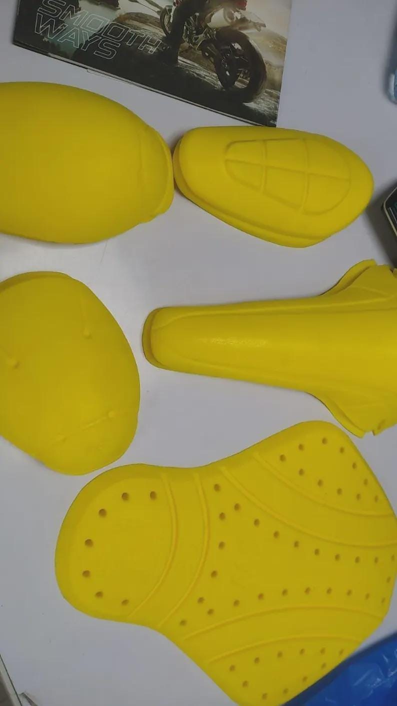 Puede incluir: Equipo de protecci&oacute;n para motocicletas de color amarillo brillante, que incluye protectores de hombros y espalda. Las piezas tienen varias formas y tama&ntilde;os, algunas con orificios de ventilaci&oacute;n. La imagen tambi&eacute;n muestra una revista con las palabras "SMOOTH WAYS".