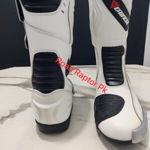 Puede incluir: Par de botas de moto blancas y negras. Las botas tienen un dise&ntilde;o alto con detalles en negro en la parte delantera y los laterales. La marca "DAINESE" es visible en la parte superior de la bota. Las botas est&aacute;n dise&ntilde;adas para protecci&oacute;n y estilo.