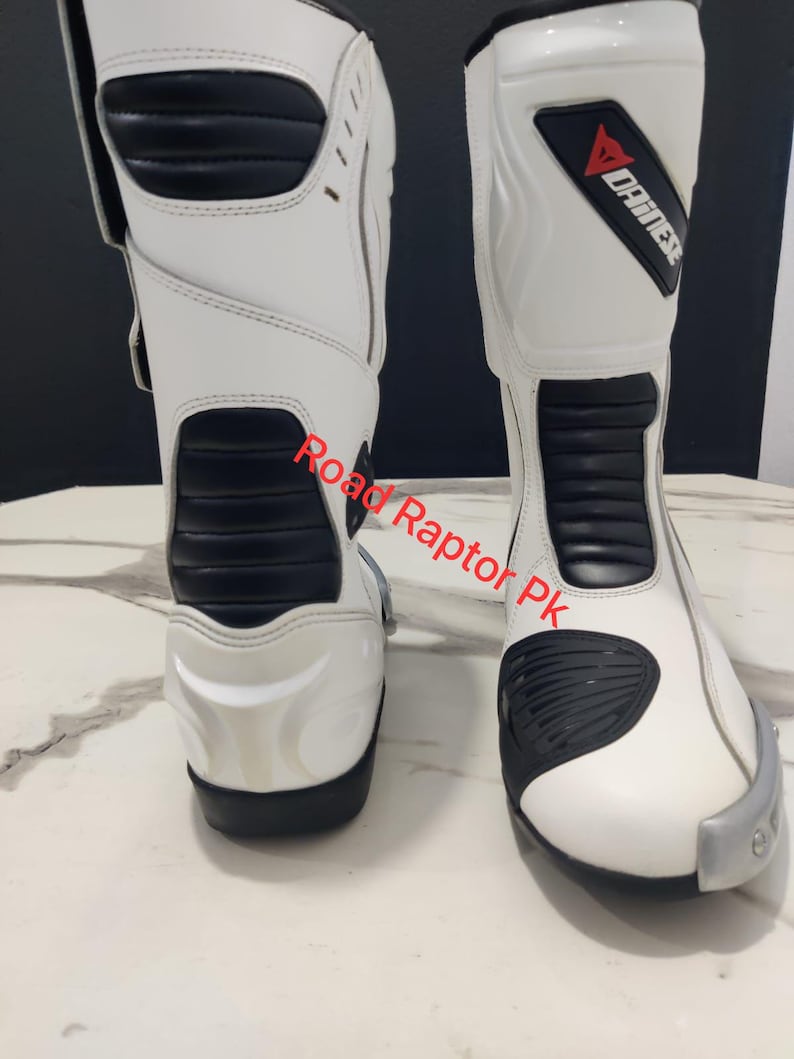 Puede incluir: Par de botas de moto blancas y negras. Las botas tienen un dise&ntilde;o alto con detalles en negro en la parte delantera y los laterales. La marca "DAINESE" es visible en la parte superior de la bota. Las botas est&aacute;n dise&ntilde;adas para protecci&oacute;n y estilo.