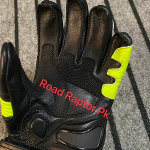 May include: Black motorcycle gloves with neon yellow accents. The gloves have a padded design and the text "Road Raptor Pk" is visible. The gloves are made of leather and have a reinforced palm area.