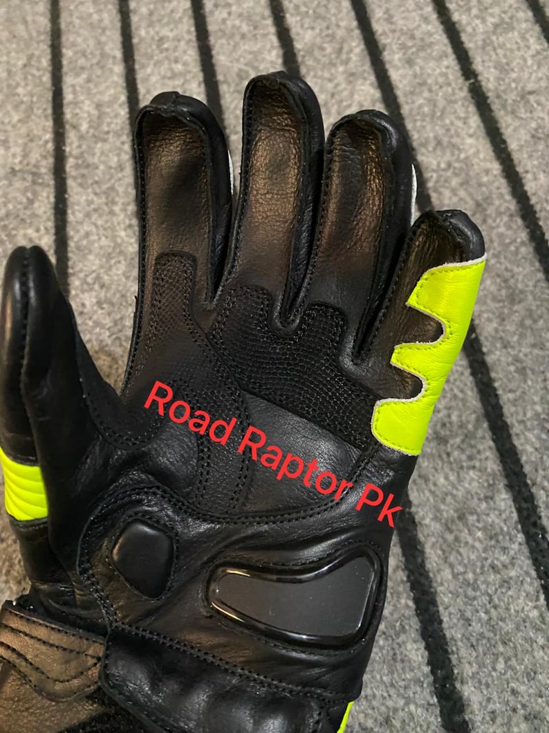 May include: Black motorcycle gloves with neon yellow accents. The gloves have a padded design and the text "Road Raptor Pk" is visible. The gloves are made of leather and have a reinforced palm area.