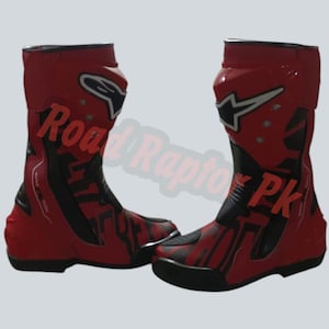May include: Pair of red and black motorcycle boots. The boots have a high-top design with a prominent white star logo and the text "Road Raptor PK". The boots are made of a glossy material.