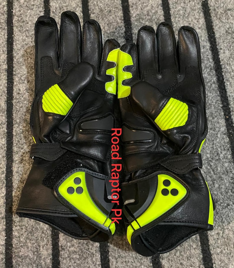 May include: Pair of black motorcycle gloves with neon yellow accents. The gloves feature reinforced knuckles and a velcro wrist strap. The text "Road Raptor Pk" is printed vertically on the gloves.