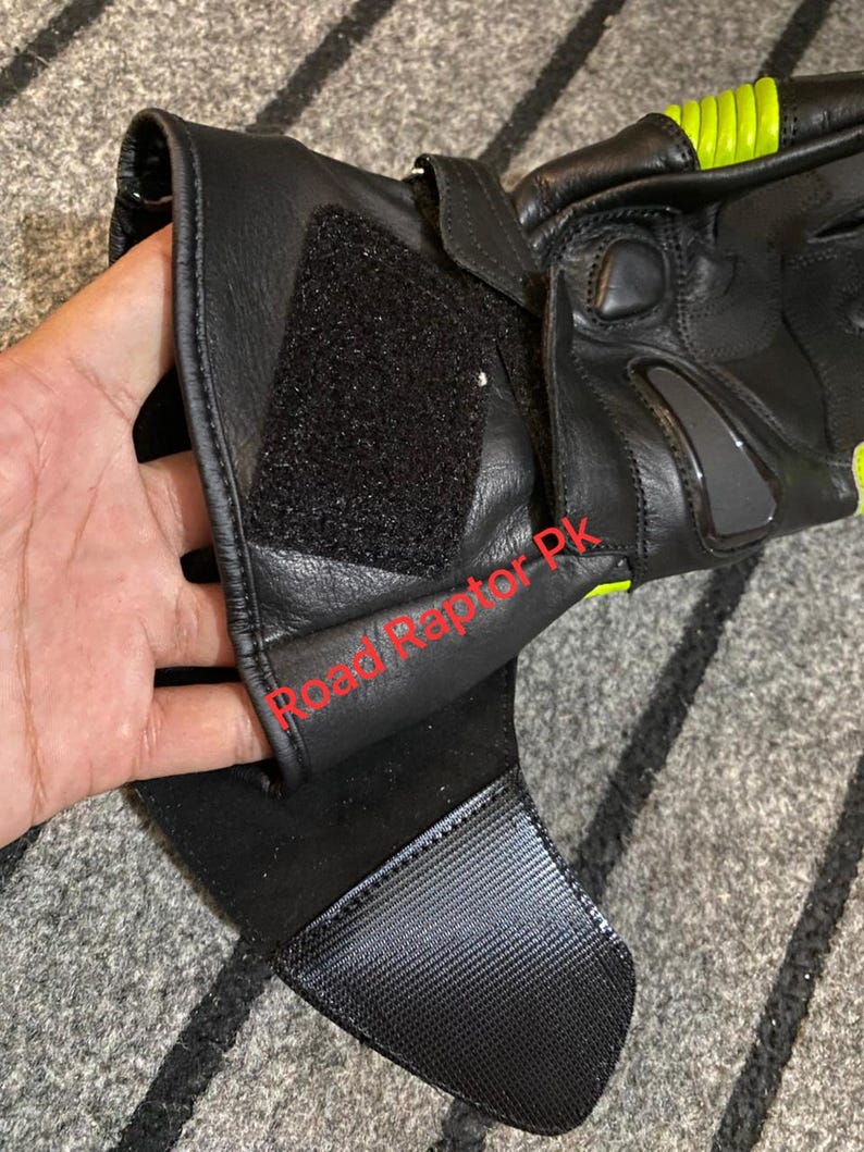 May include: Black motorcycle gloves with neon yellow accents. The gloves feature a hook and loop closure and a textured palm for grip. The gloves have a padded design for protection and are made of leather.
