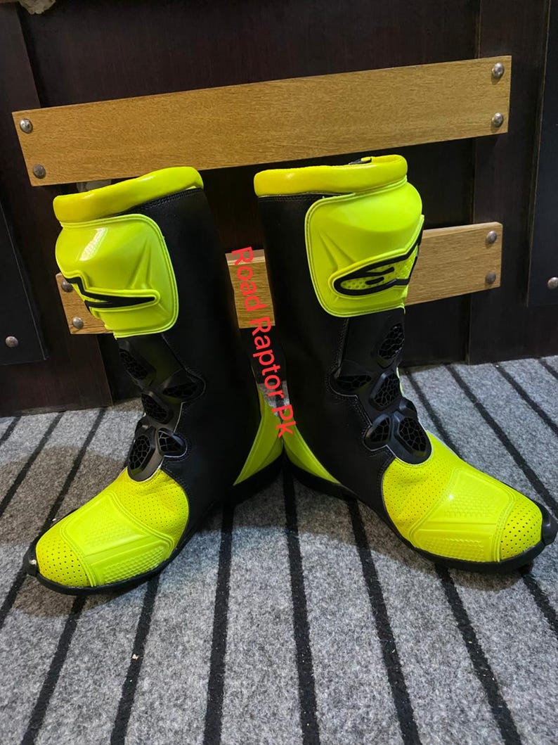 May include: Pair of black and neon yellow motorcycle boots. The boots have a high-top design with protective panels on the shin and ankle. The toe and heel areas are reinforced. The boots are designed for safety and performance.