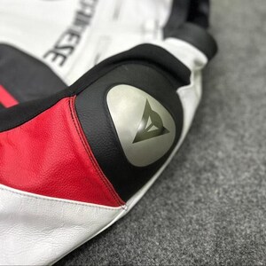 Puede incluir: Primer plano de una secci&oacute;n de chaqueta de moto. La chaqueta presenta paneles de cuero blanco, negro y rojo. Un emblema plateado con un dise&ntilde;o triangular es visible en la secci&oacute;n negra. La costura es visible.