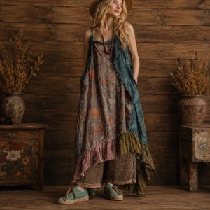 May include: A sleeveless, floor-length dress featuring a layered, multi-colored fabric with a textured, distressed appearance. The garment includes a ruffled hemline in shades of pink and olive green, worn over wide-leg, brown textured trousers.