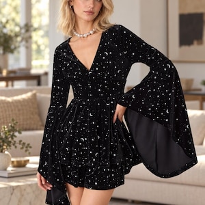 May include: A black velvet two-piece set featuring a peplum top with a deep V-neckline and long, wide bell sleeves, paired with matching shorts. The fabric is decorated with a repeating silver-toned pattern of crescent moons and stars.