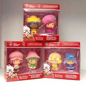 May include: Four boxed sets of Strawberry Shortcake flocked figures. Each box contains two figures, including Orange Blossom, Raspberry Tart, Strawberry Shortcake, Lime Chiffon, Lemon Meringue, and Blueberry Muffin. The boxes are red.