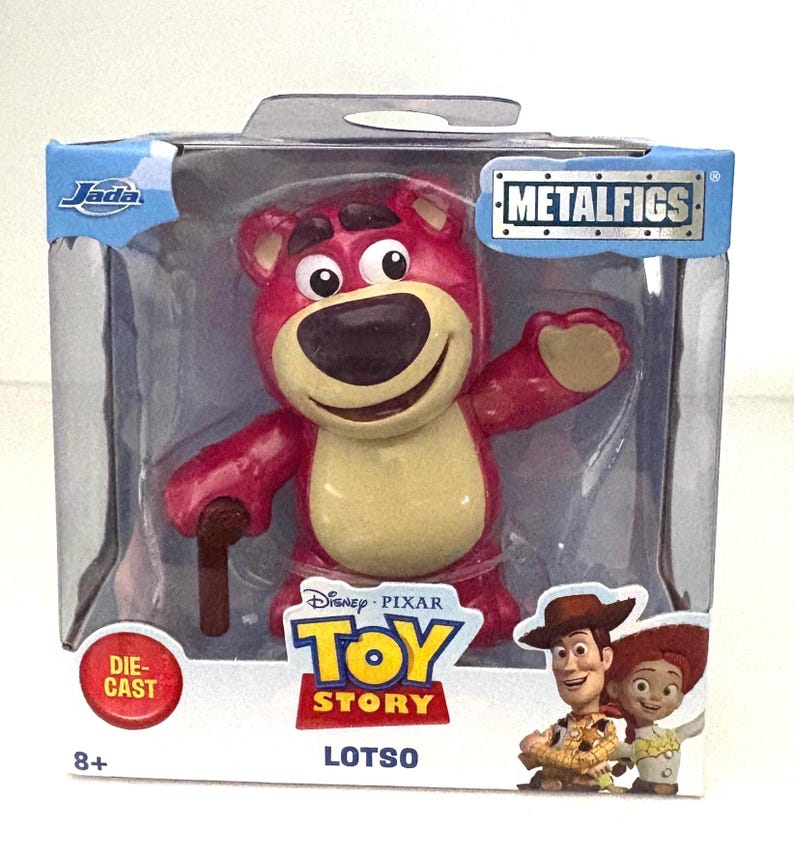 May include: A die-cast Lotso figure from Disney Pixar's Toy Story, packaged in a clear plastic box. The figure is a pink bear with a tan belly, holding a brown cane. The packaging includes the Metalfigs logo and the Toy Story logo.