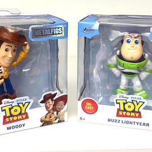 May include: Two die-cast metal figures of Woody and Buzz Lightyear from Disney Pixar's Toy Story, in their original packaging. Woody is in a yellow shirt, blue pants, and a brown hat. Buzz Lightyear is in a white and green spacesuit.