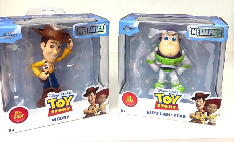 May include: Two die-cast metal figures of Woody and Buzz Lightyear from Disney Pixar's Toy Story, in their original packaging. Woody is in a yellow shirt, blue pants, and a brown hat. Buzz Lightyear is in a white and green spacesuit.