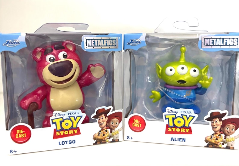 May include: Two die-cast metal figures from the Disney Pixar Toy Story franchise. One is Lotso, a pink bear with a cane. The other is an Alien, a green three-eyed character in a blue suit. Both are in their original packaging.