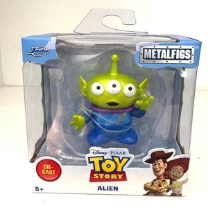 May include: A die-cast Toy Story Alien figure in a clear plastic package. The green alien has three eyes, a purple collar, and blue clothing. The package includes the Toy Story logo, the word "Alien", and images of Woody and Jessie.
