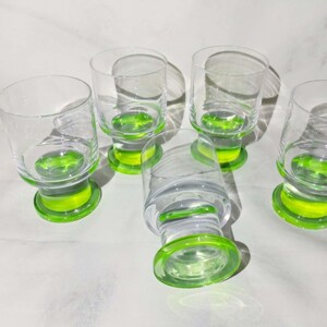Könnte beinhalten: Sechs klare Trinkgläser mit einem leuchtend grünen Boden. Die Gläser haben ein schlichtes, elegantes Design, ideal zum Servieren von Getränken. Der grüne Boden verleiht dem Glas einen Farbtupfer.